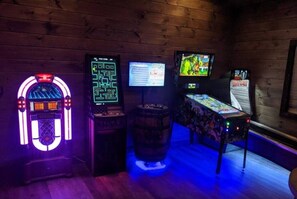A room with wooden walls, a neon jukebox, a digital jukebox, a video game console, and a barrel. - SerenityLod: POOL, Theater, Games, HotTub, Wi-Fi, Pets (Sevierville)