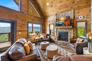 A cozy cabin interior with a stone fireplace, leather sofas, and a view of the mountains. - SerenityLod: POOL, Theater, Games, HotTub, Wi-Fi, Pets (Sevierville)