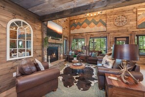 L’intérieur d’une cabane en rondins, avec une cheminée, des canapés en cuir, un tapis en peau de vache et une grande fenêtre donnant sur la forêt.