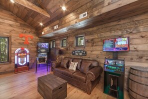 Ein Holzinnenraum mit einem braunen Ledersofa, Spielautomaten und einem Fernseher.