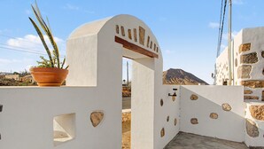 A white building with a stone facade, a potted plant, and a mountain in the background. - Casa Clarita: House with Mountain Views, Private Terrace, and Wi-Fi (Tindaya)