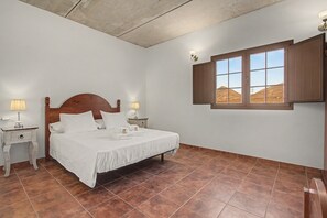 A bedroom with a bed, two bedside tables, a window with wooden shutters, and a view of hills. - Casa Clarita: House with Mountain Views, Private Terrace, and Wi-Fi (Tindaya)