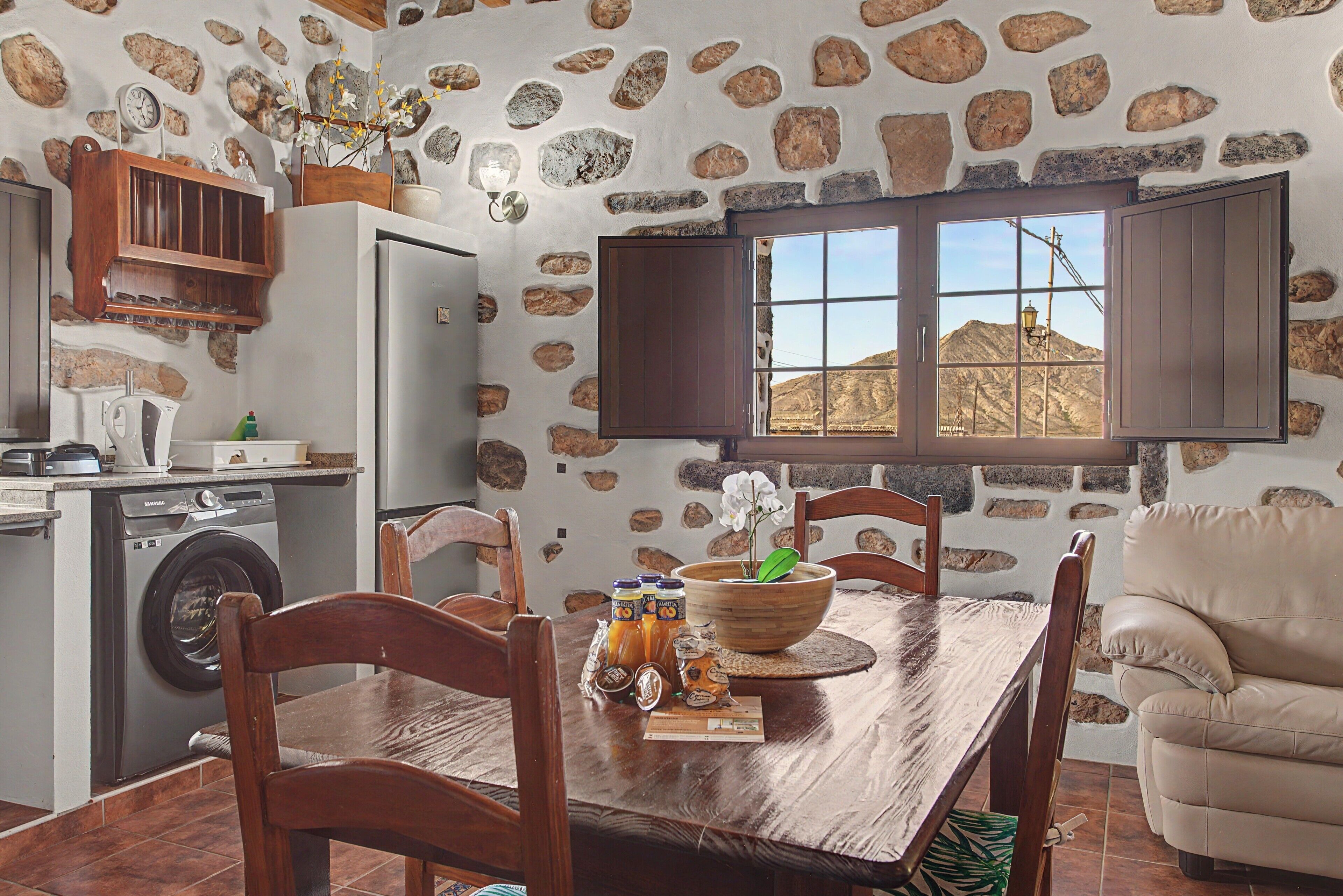 Eine Küche mit einer Steinwand, Holzschränken, einem Kühlschrank und einem Esstisch mit Stühlen.