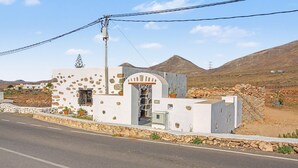 A white building with a stone facade, a small entrance, and a mountainous backdrop. - Casa Clarita: House with Mountain Views, Private Terrace, and Wi-Fi (Tindaya)