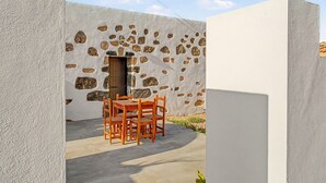 A patio with a table and chairs, a stone wall, and a door. - Casa Clarita: House with Mountain Views, Private Terrace, and Wi-Fi (Tindaya)