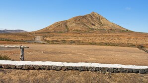 A mountainous landscape with a dirt road leading to a settlement. - Casa Clarita: House with Mountain Views, Private Terrace, and Wi-Fi (Tindaya)