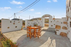 A patio with a wooden table and chairs, a white wall with stone accents, and a gate leading to a property. - Casa Clarita: House with Mountain Views, Private Terrace, and Wi-Fi (Tindaya)