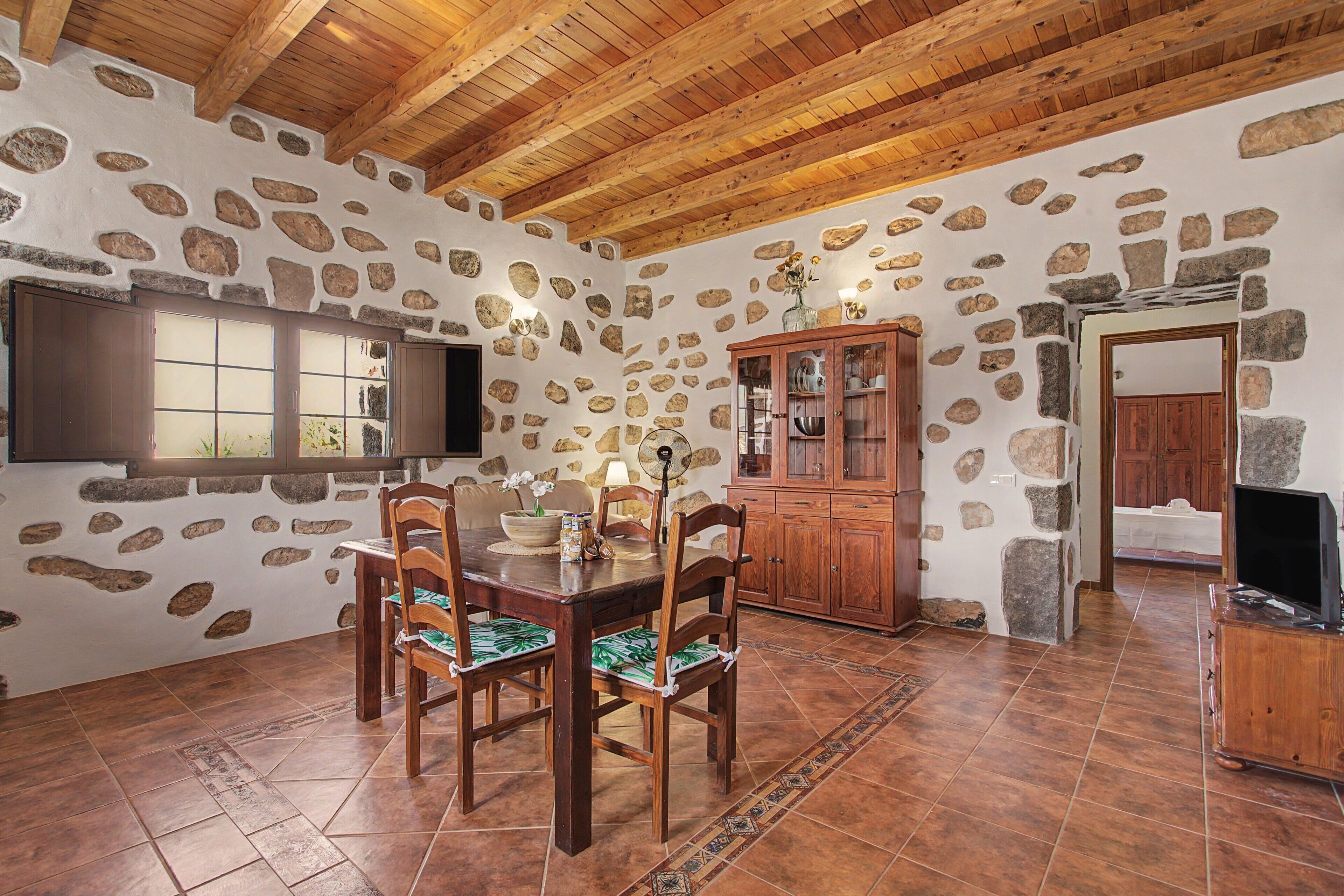 A dining area with a stone wall, wooden ceiling, and a dining table with chairs.