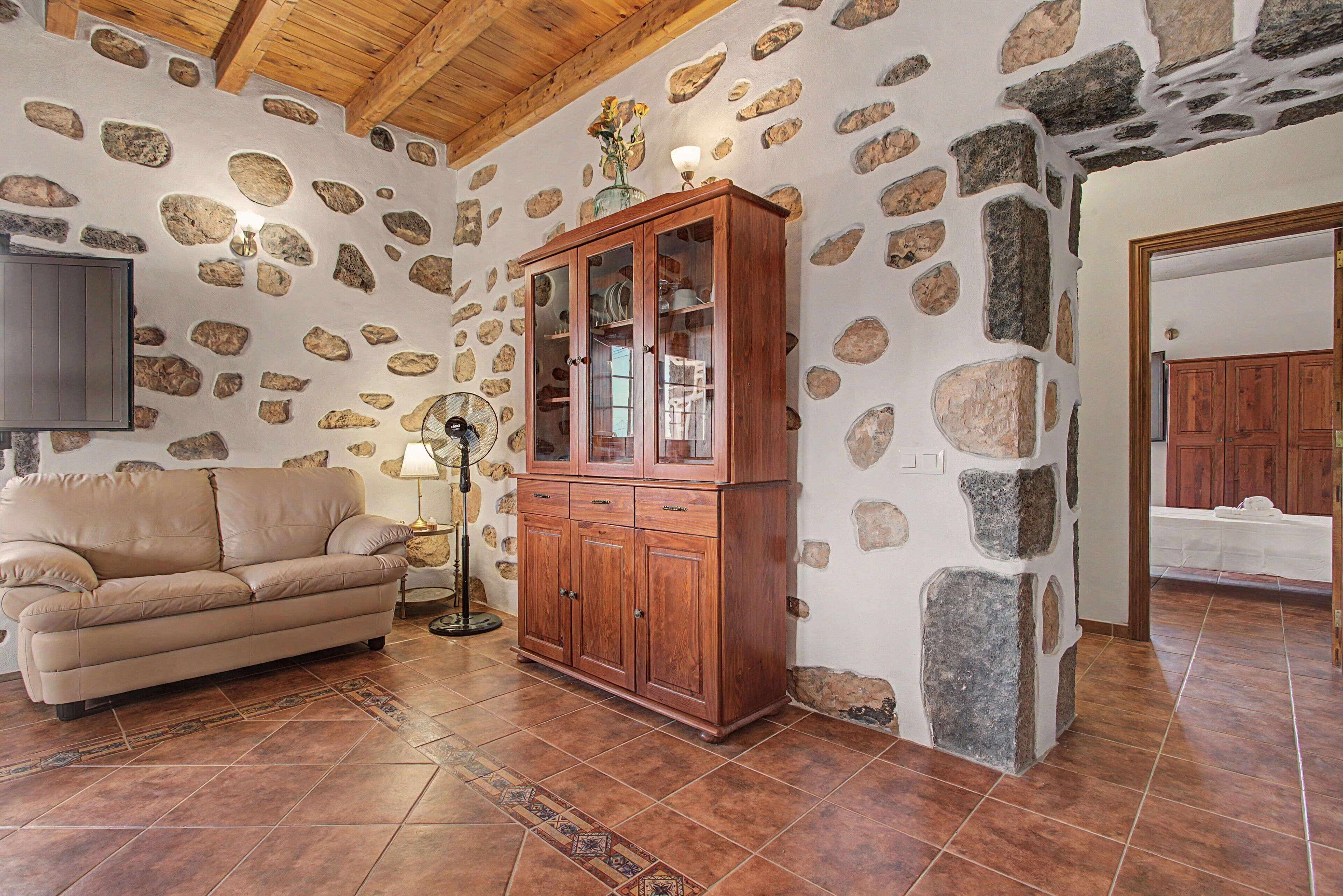 A room with a stone wall, a wooden cabinet, a beige sofa, and a tiled floor.