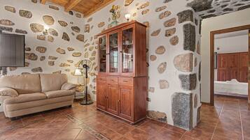 A room with a stone wall, a wooden cabinet, a beige sofa, and a tiled floor.