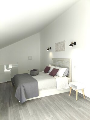 Ein modernes Schlafzimmer mit schrägem Dach, einem Bett mit weißer Bettwäsche und zwei Kissen, einem Nachttisch und zwei Wandlampen.