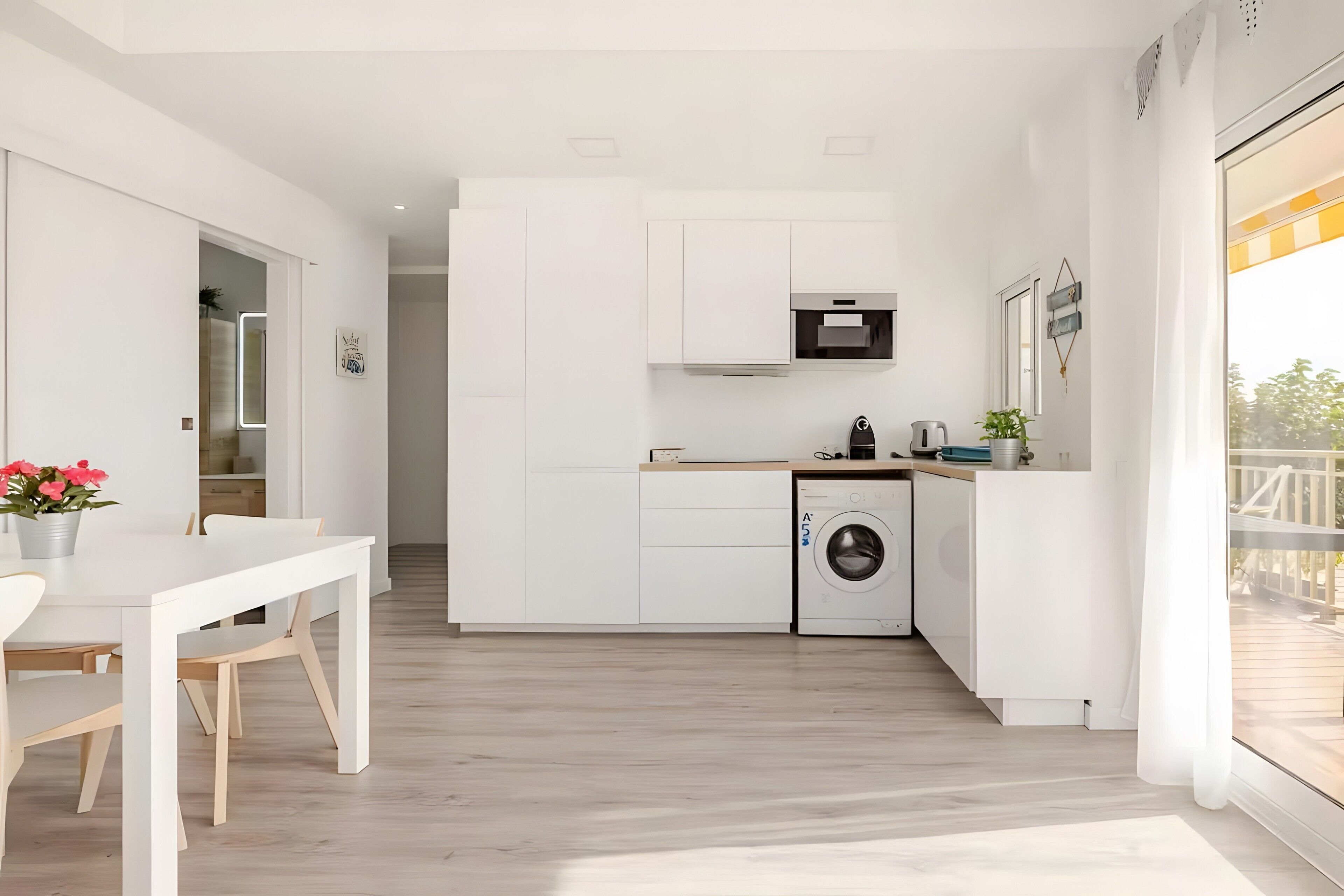 Een moderne keuken met witte kastjes, een ingebouwde wasmachine en een eethoek met een tafel en stoelen.