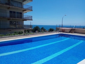 Una piscina con agua azul cristalina, vista al mar y un edificio con balcones.