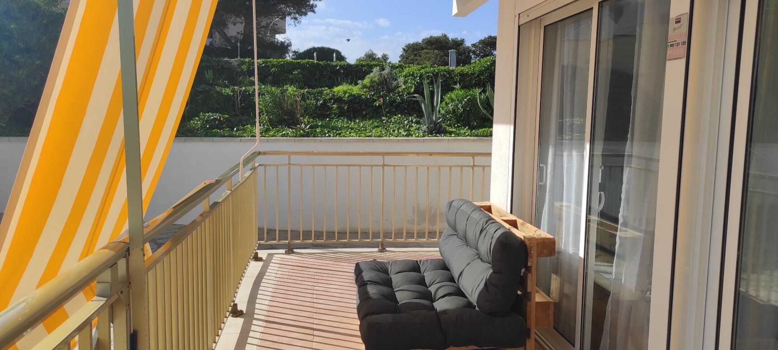 Een balkon met een houten vloer, een met kussens beklede bank en een geel gestreept zonnescherm.