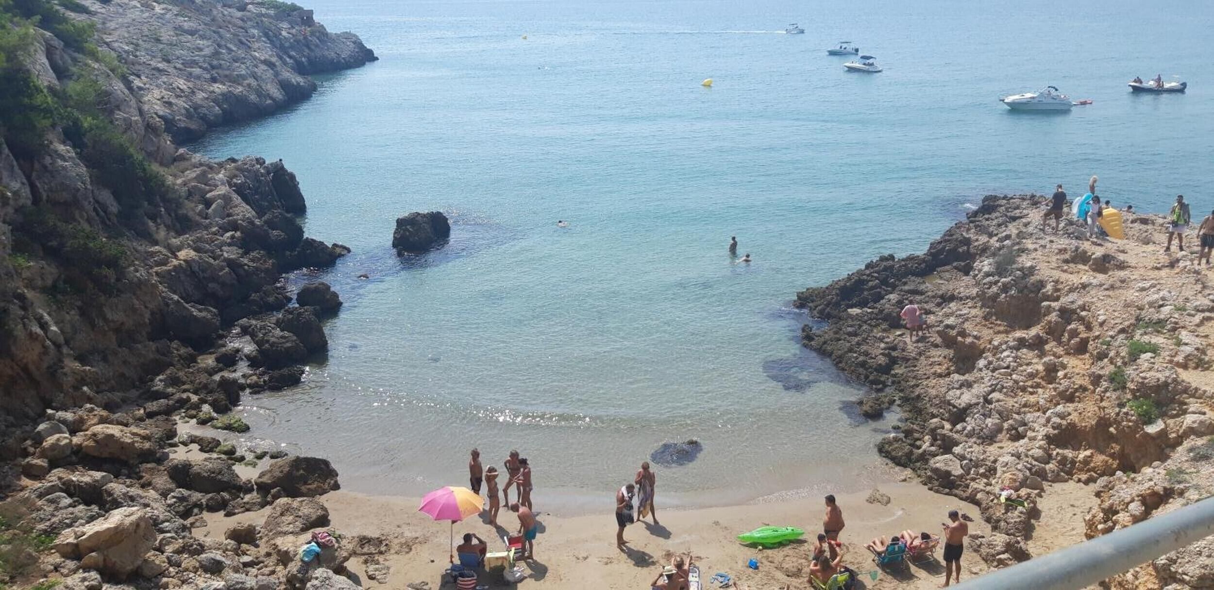 A rocky coastal area with clear water, boats, and people.