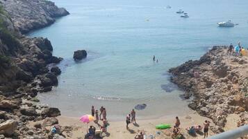 A rocky coastal area with clear water, boats, and people.