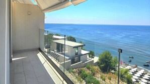 Uma varanda com vista para o mar, um edifício moderno e uma praia com guarda-sóis.