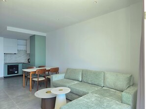 A modern living room with a sectional sofa, a dining table with chairs, and a kitchen area in the background. - Panorama Deep Blue 001 (Shengjin)