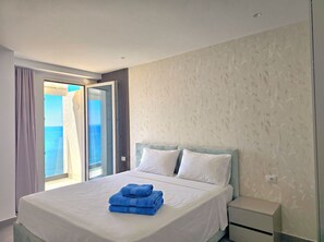 A hotel room with a bed, a nightstand, and a view of the sea through a window. - Panorama Deep Blue 001 (Shengjin)