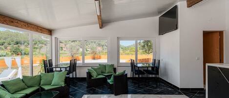 A spacious room with a large window, a flat-screen TV, and a dining area with chairs and a table.