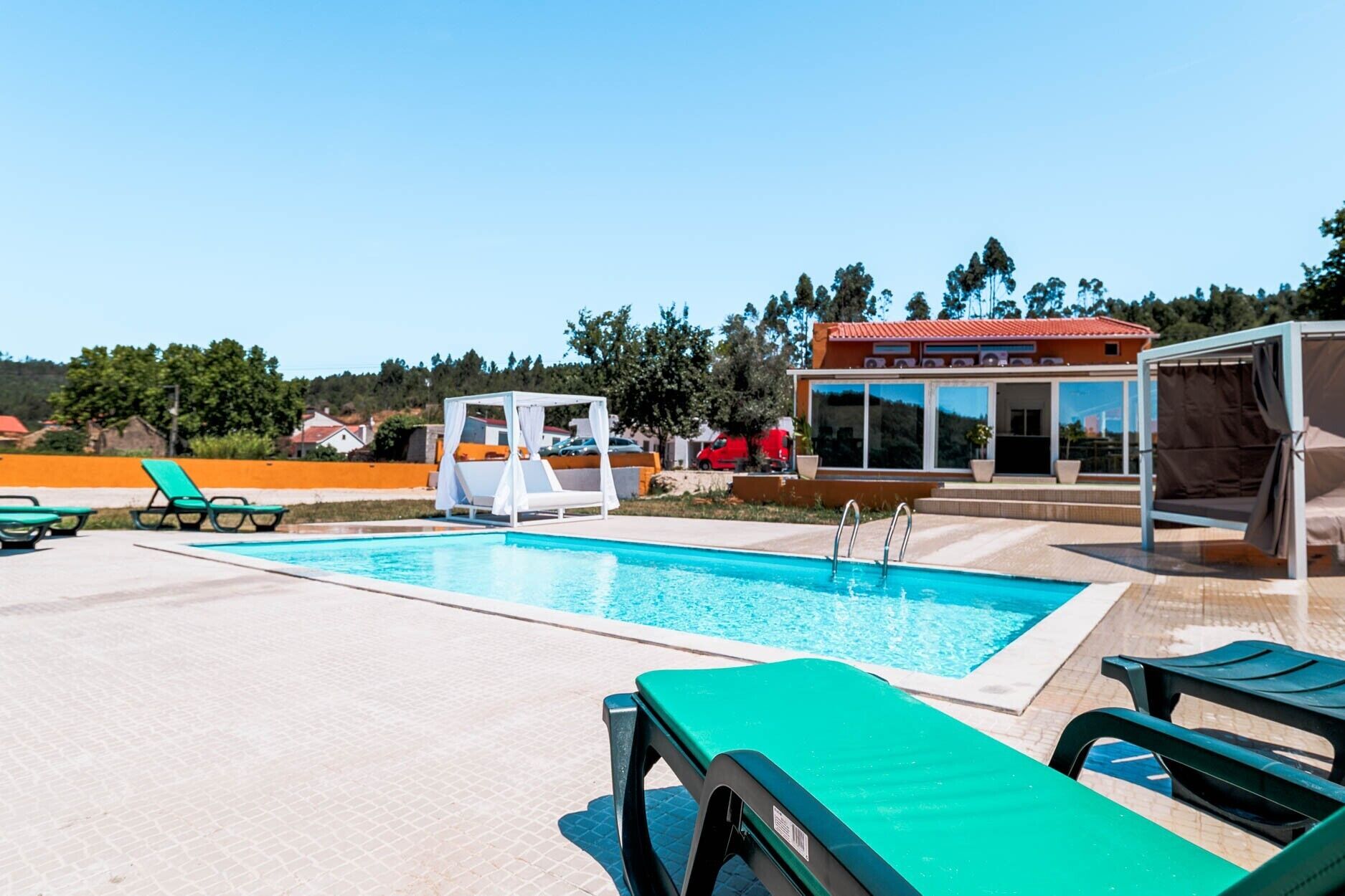 A swimming pool with lounge chairs, a cabana, and a building with large windows.