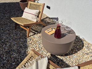 A sunlit outdoor seating area with a round table, a wicker chair, and a cushion.
