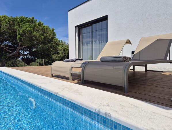 A modern outdoor pool area with lounge chairs and a wooden deck.