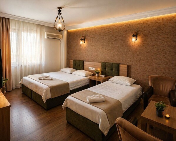 A hotel room with two beds, a wooden floor, a brick accent wall, and a ceiling light fixture.