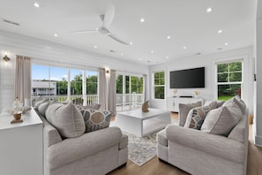 A modern living room with a large TV, comfortable seating, and a view of the outdoors.