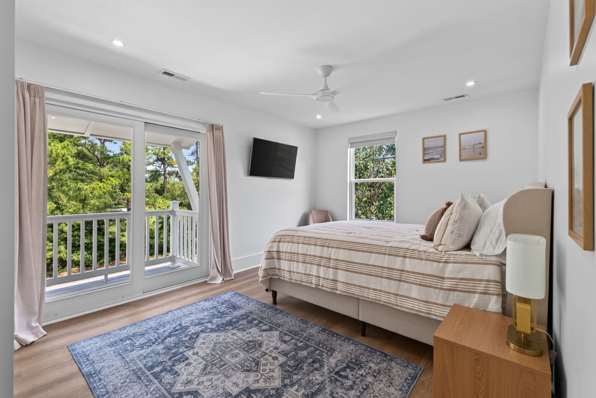 A bedroom with a bed, a TV, a ceiling fan, a window, and a balcony.