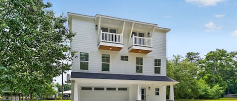 A two-story residential building with a garage, a covered front porch, and a small front yard.