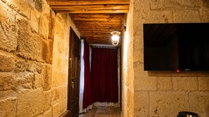 A narrow stone-walled hallway with a wooden ceiling, a red curtain, and a mounted television. - La Mar Cave Cappadocia (Ürgüp)