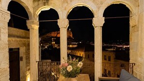 An outdoor seating area with a wooden table and chairs, a vase with flowers, and a view of the city at night. - La Mar Cave Cappadocia (Ürgüp)