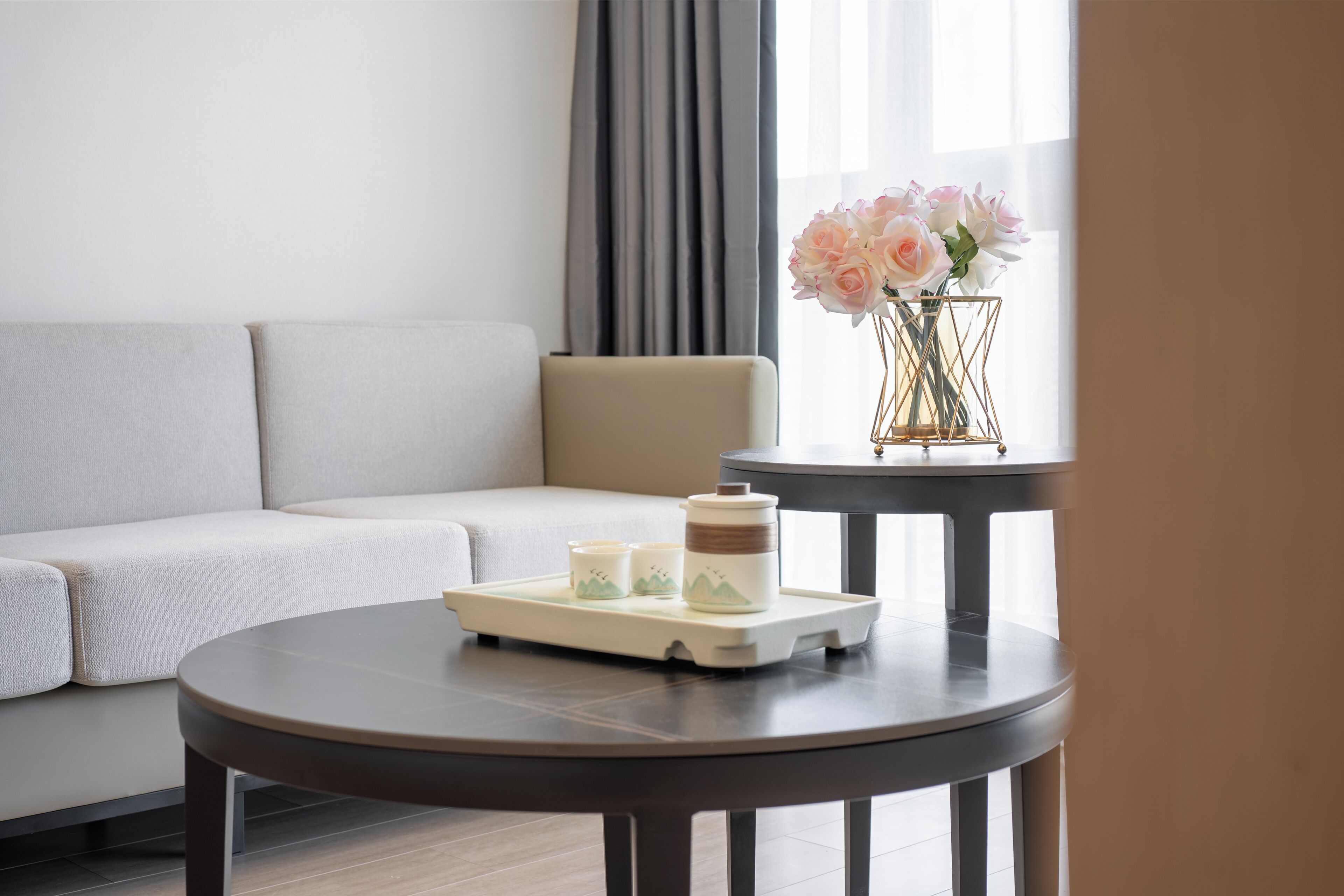 Una habitación de hotel moderna con un sofá, una mesita redonda con una bandeja y un jarrón con flores.