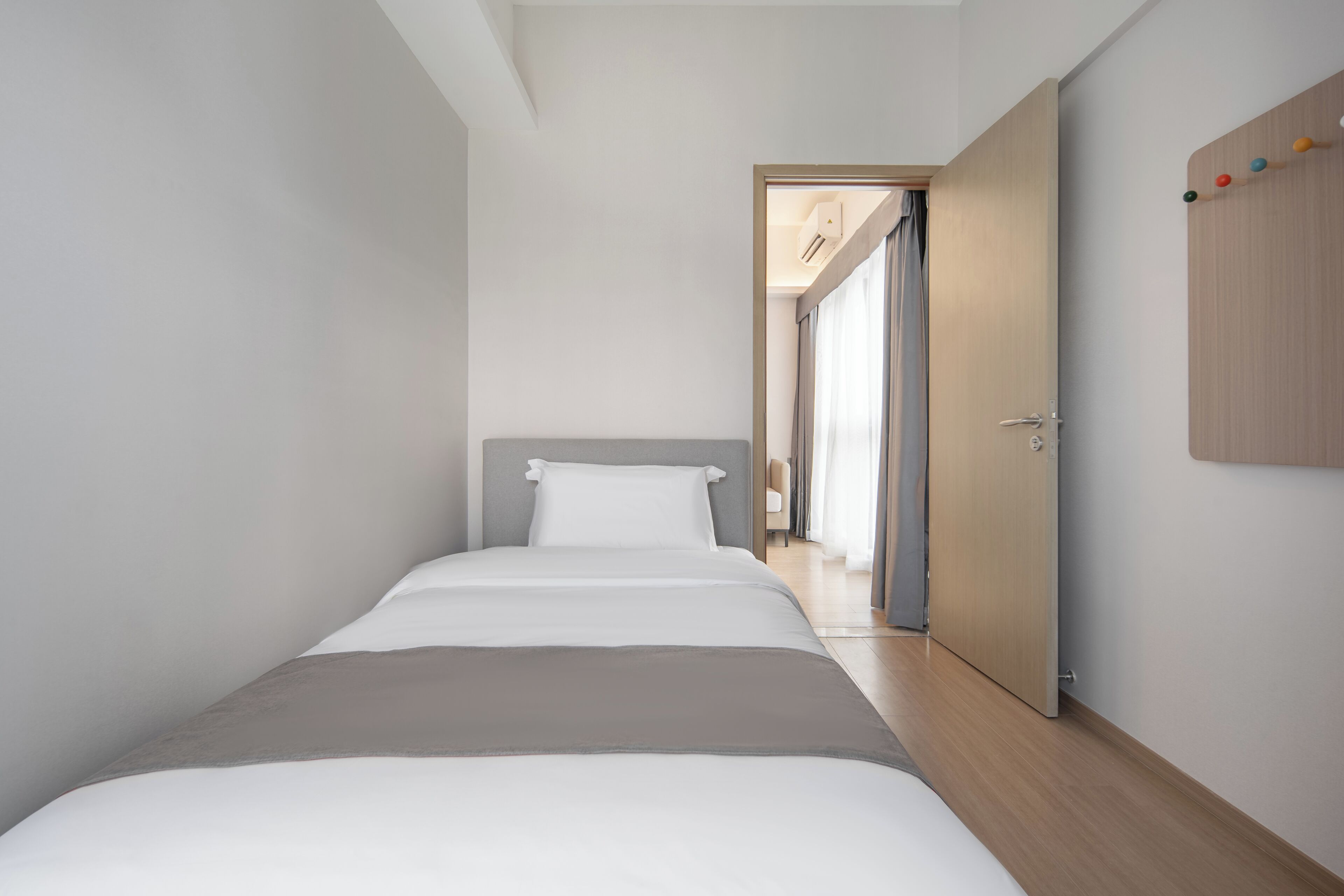 Habitación de hotel moderna con una cama individual, una puerta de madera y vistas al pasillo.