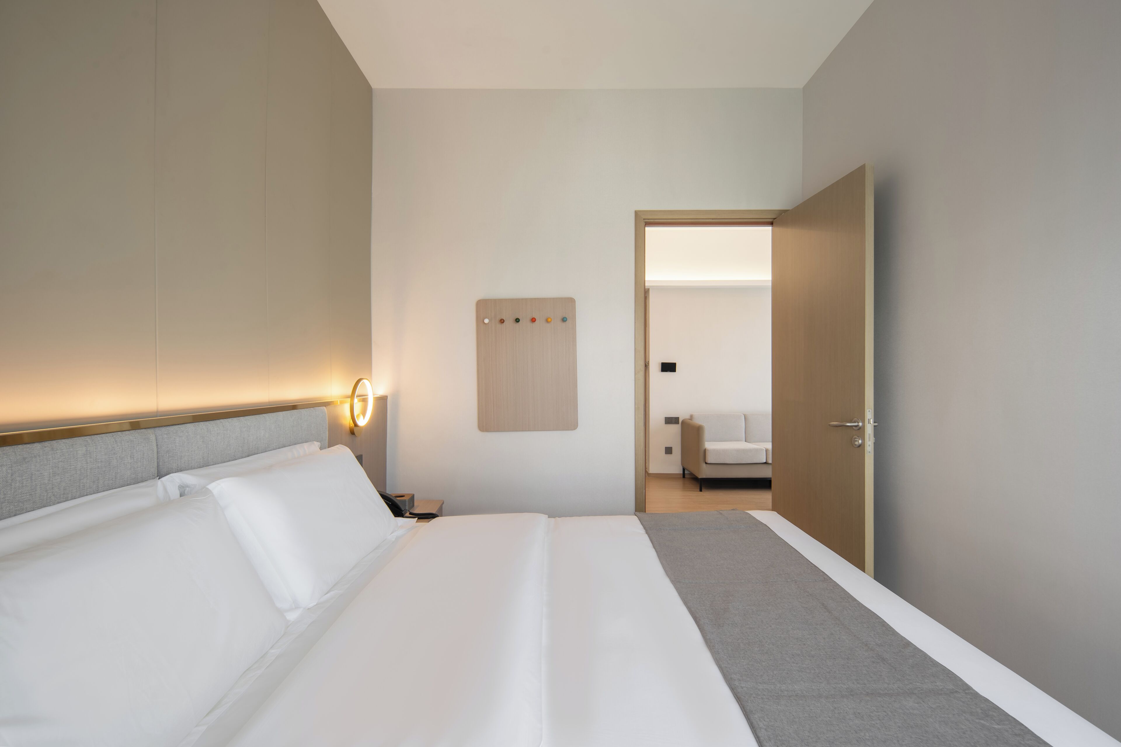 A hotel room with a bed, bedside table, and a wall-mounted control panel.