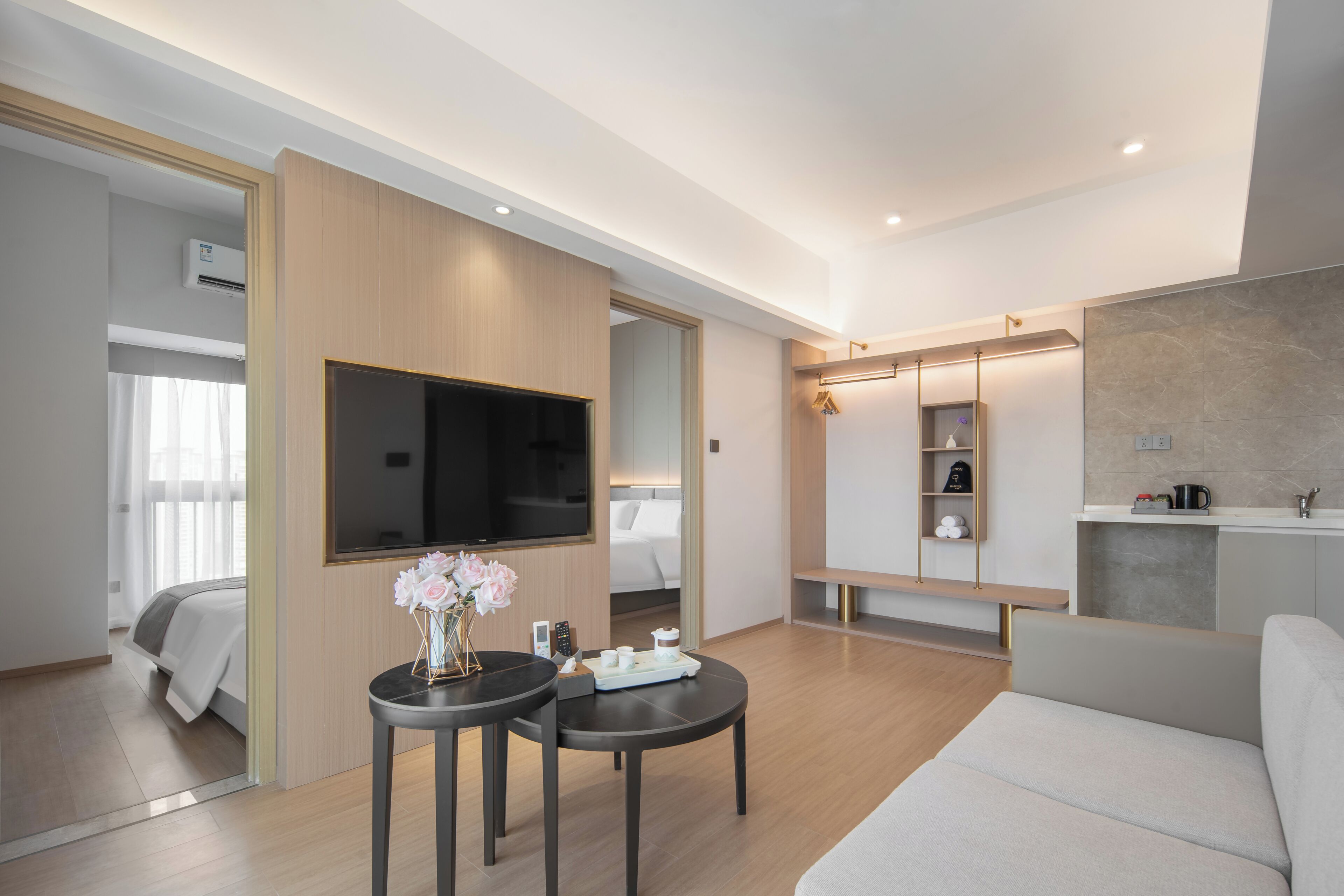 A modern hotel room with a flat-screen TV, a sofa, a dining table, and a kitchen area.