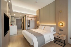 A modern hotel room with a large bed, bedside tables, a TV, and a walk-in closet.