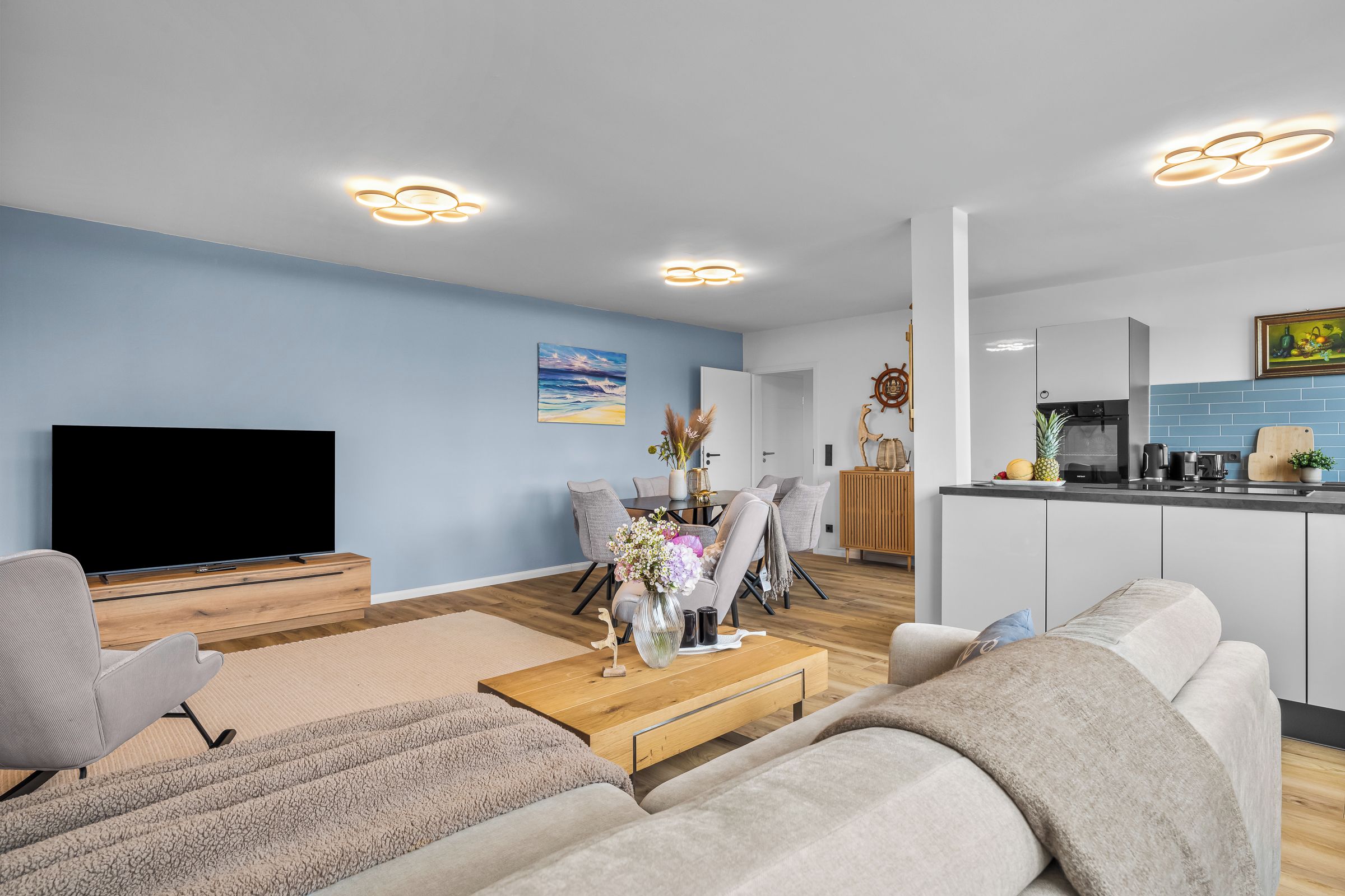Ein modernes Wohnzimmer mit Fernseher, einer Couch, einem Couchtisch und einem Essbereich mit Stühlen sowie einer Blumenvase.