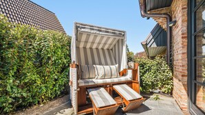 Une chaise de plage avec un parasol à rayures, un banc en bois et un mur de briques en arrière-plan.