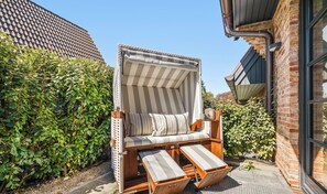 Une chaise de plage avec un parasol à rayures, un banc en bois et un mur de briques en arrière-plan.