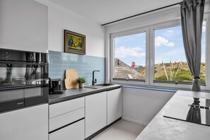 Una cocina moderna con estufa negra, armarios blancos y ventana con vistas al campo.