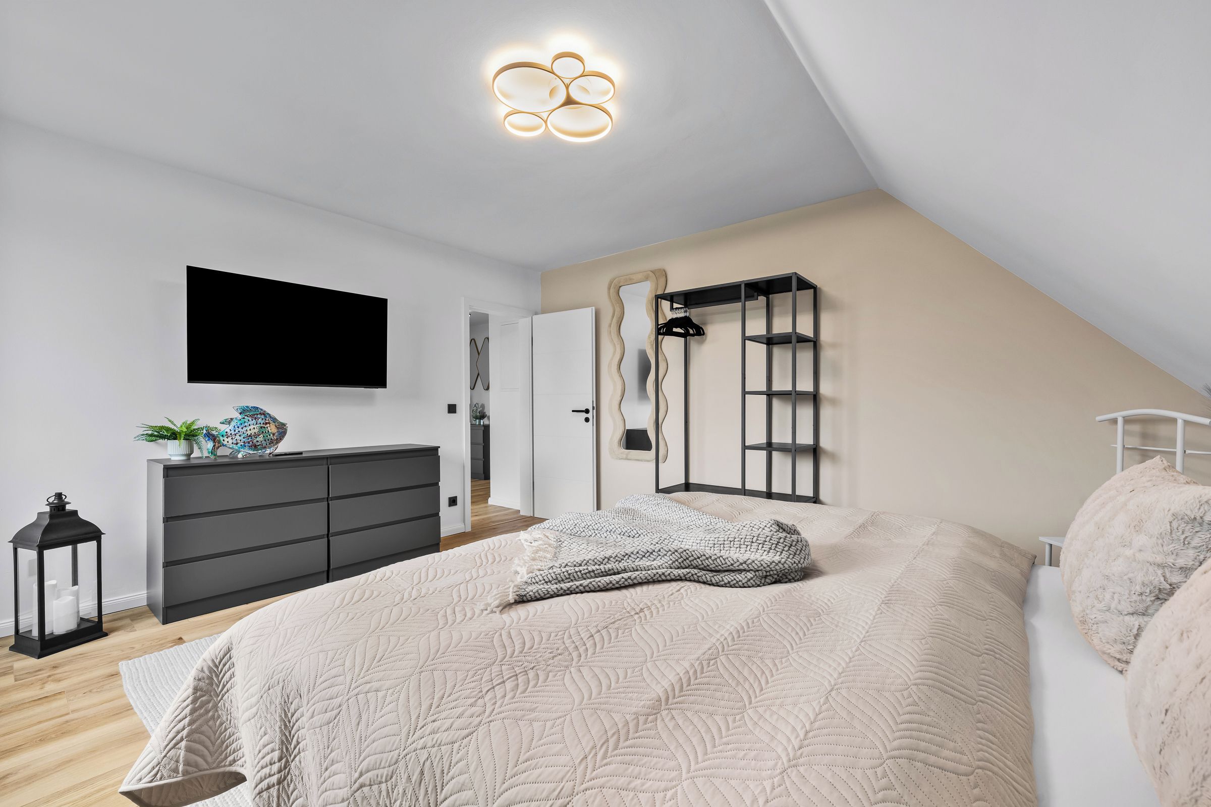 A modern bedroom with a bed, dresser, and a TV mounted on the wall.
