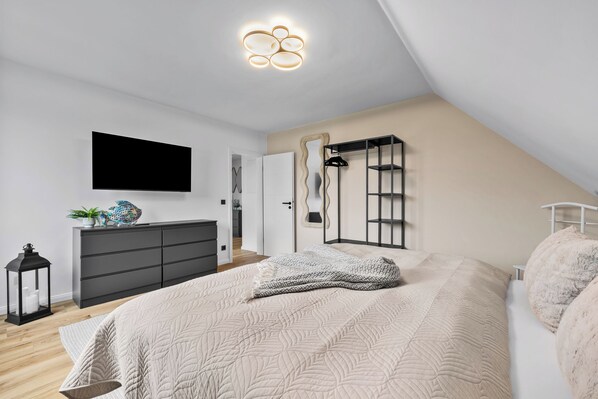 Un dormitorio moderno con cama, cómoda y televisor montado en la pared.