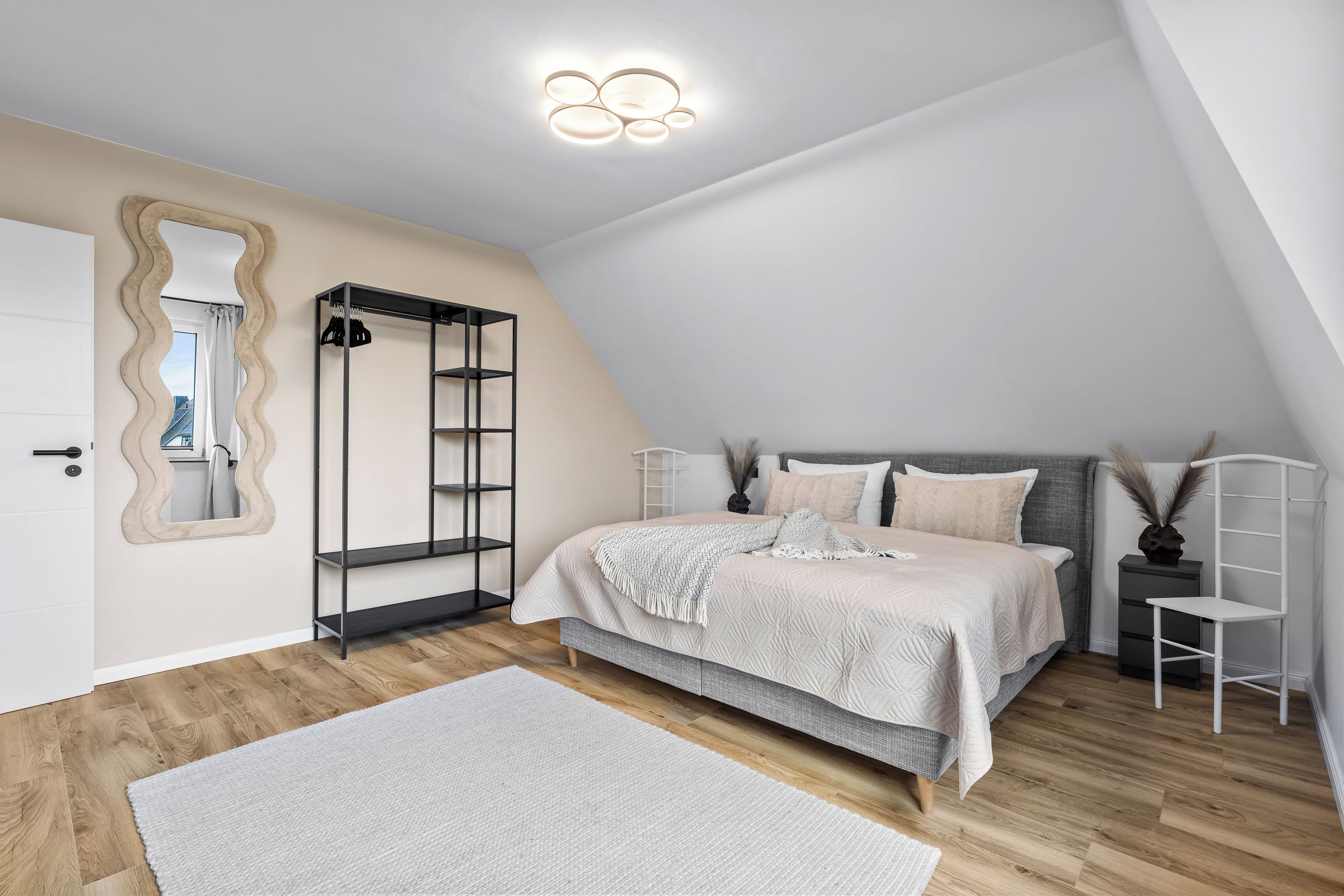 Ein Schlafzimmer mit Bett, Kleiderschrank, Spiegel und einer Deckenleuchte.