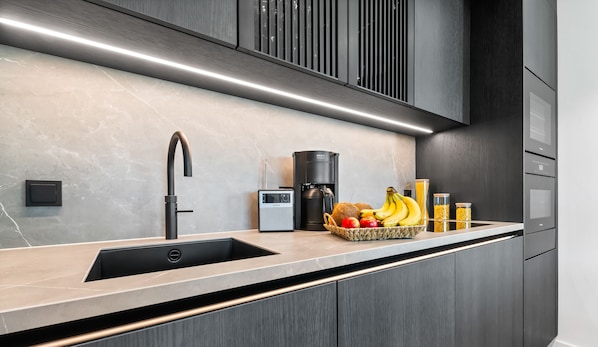 Une cuisine moderne avec un robinet noir élégant, une machine à café Krups et un panier de fruits posé sur le plan de travail.