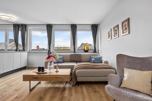 Una sala de estar moderna con un sofá, una mesa de centro y vistas a la playa a través de amplias ventanas.