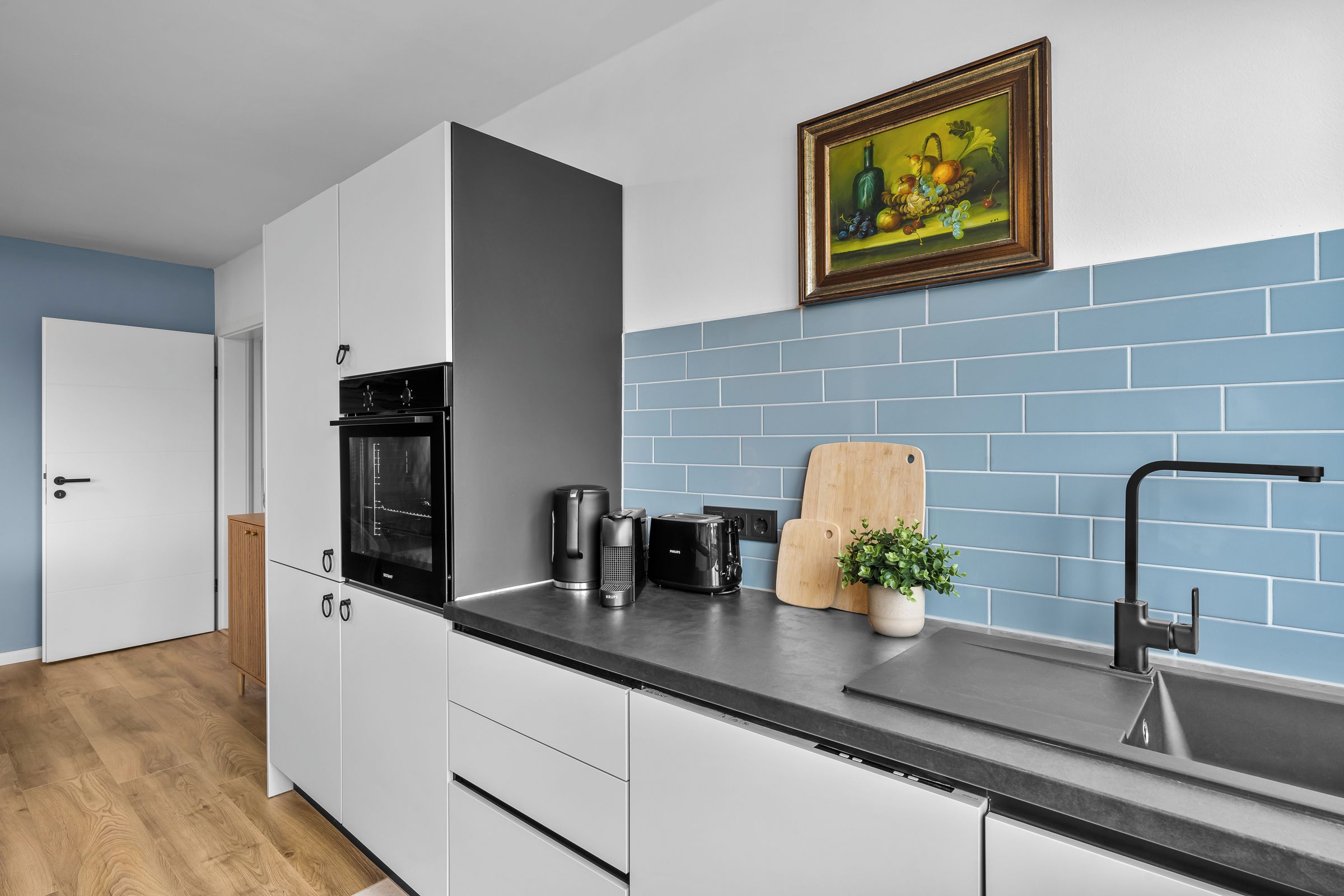 Eine moderne Küche mit weißen Schränken, einer schwarzen Arbeitsplatte, einer Kaffeemaschine, einem Toaster und einem Holzschneidebrett.