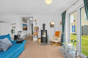 Een moderne woonkamer met een blauwe bank, een glazen salontafel, een open haard en uitzicht naar buiten.