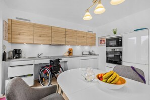 Een moderne keuken met houten kastjes, een Bosch magnetron en een rolstoel in de hoek.